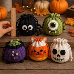 Könnte beinhalten: Fünf gehäkelte Beutel mit Kordelzug und Halloween-Motiven: eine schwarze Spinne, ein grünes einäugiges Monster, ein violetter Kessel mit grünen Blasen, eine Candy-Corn-Katze und ein weißer Totenkopf. Ein Holzlineal zeigt, dass die Spinne 7,5 cm groß ist.