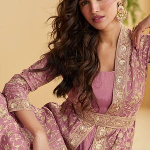May include: A mauve outfit comprising a square-neck top and a long jacket with gold embroidery. The jacket's edges and belt feature detailed gold patterns. The ensemble is completed with matching trousers and gold jewellery.