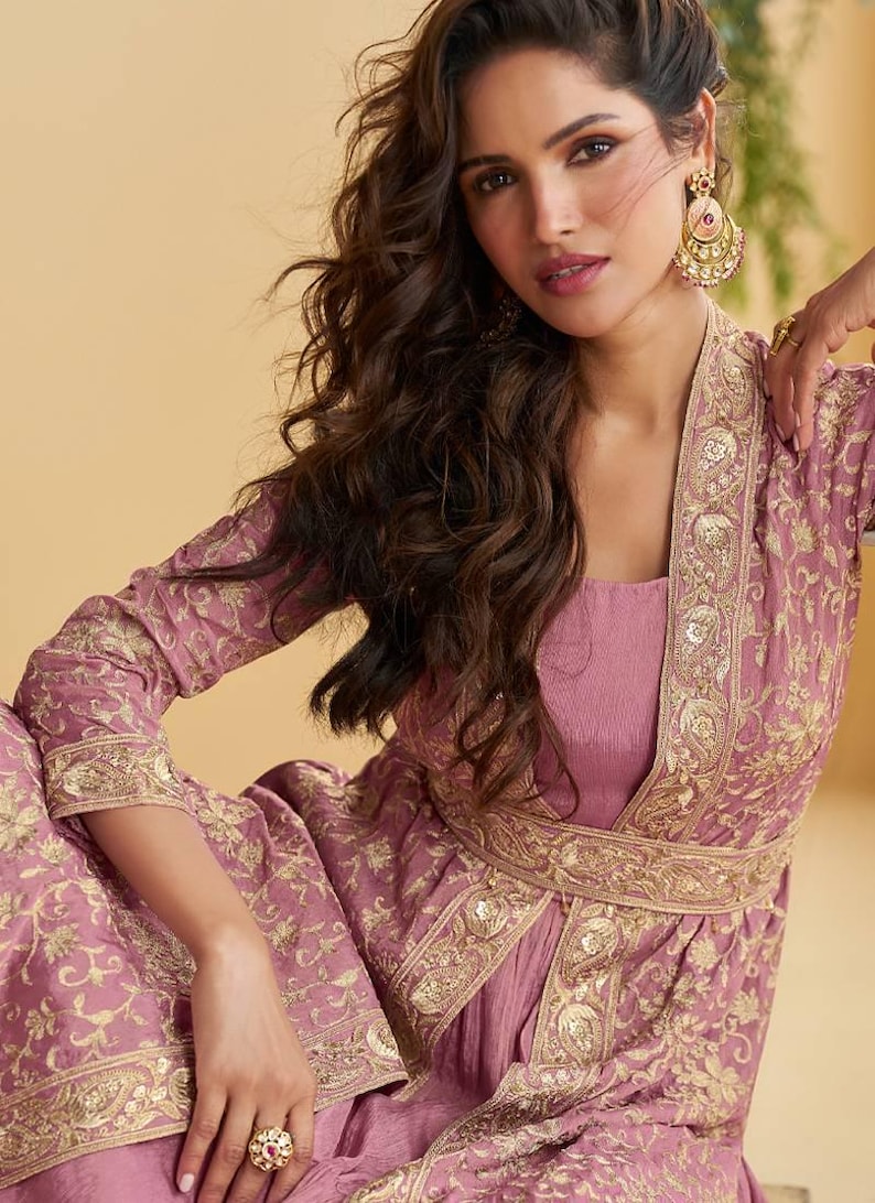 May include: A mauve outfit comprising a square-neck top and a long jacket with gold embroidery. The jacket's edges and belt feature detailed gold patterns. The ensemble is completed with matching trousers and gold jewellery.