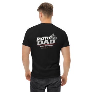 Könnte beinhalten: Ein schwarzes kurzärmeliges T-Shirt mit einer weißen Grafik auf der Rückseite. Das Design enthält den Text MOTO DAD, den Schriftzug BUILT DIFFERENT und die Worte RIDE SUPPORT REPEAT sowie eine Abbildung einer Person auf einem Motorrad.