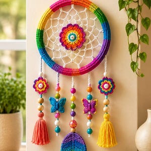 Op de afbeelding: Een ronde wandhanger met een gehaakte ring in regenboogkleuren, een wit web en een centrale regenboogbloem. De hanger is versierd met twee gehaakte bloemen, twee vlinders, een regenboogblad en twee kwastjes die naar beneden hangen.