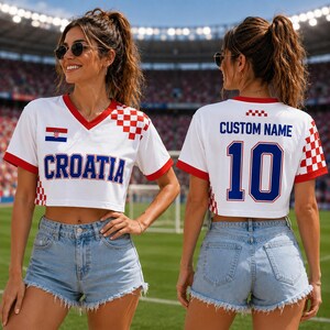 May include: A white cropped V-neck jersey with red trim and a red and white checkered pattern on the sleeves. The front features the text CROATIA and a small flag. The back displays the text CUSTOM NAME and the number 10 in blue with red outlines.