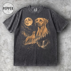 May include: A charcoal grey short-sleeve t-shirt featuring a gold-toned graphic of two dogs in a forest landscape under a full moon. The design includes a large dog portrait and a smaller dog standing on a cliff near a waterfall. The text PEPPER appears.