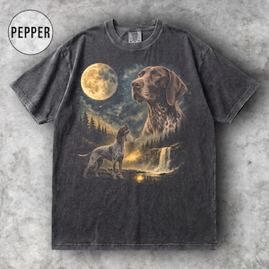 May include: A charcoal grey t-shirt featuring a graphic print of a German Shorthaired Pointer dog looking at a full moon above a forest and waterfall. The word PEPPER is printed in a circle in the upper left corner of the garment.