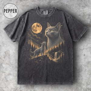 May include: A charcoal gray short-sleeve t-shirt with a graphic print featuring a large cat head, a smaller cat standing on a cliff, a full moon, a forest, and a waterfall. The text PEPPER is printed in a circle in the upper left corner.