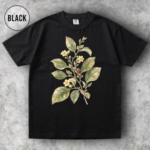 K&ouml;nnte beinhalten: Schwarzes T-Shirt mit botanischer Illustration. Das Design zeigt einen Zweig mit gr&uuml;nen Bl&auml;ttern, kleinen gelben Bl&uuml;ten und einem roten Marienk&auml;fer. Das Wort "BLACK" befindet sich in einem wei&szlig;en Kreis oben links.