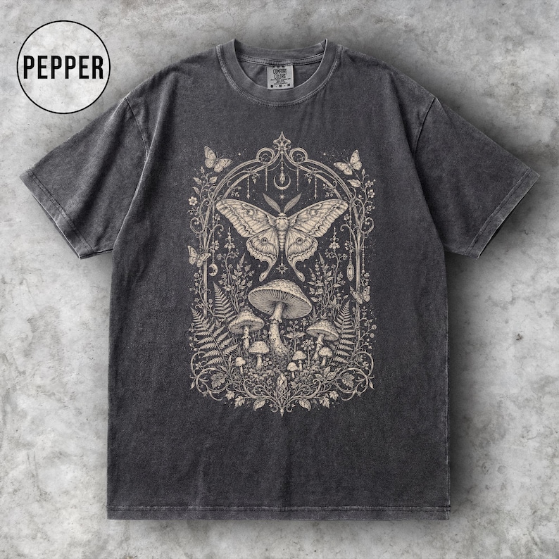 May include: Dark gray t-shirt featuring a detailed illustration of a moth, mushrooms, and foliage within an arched frame. The design is in a neutral color palette, creating a vintage aesthetic. The word "PEPPER" is in a circle in the upper left corner.