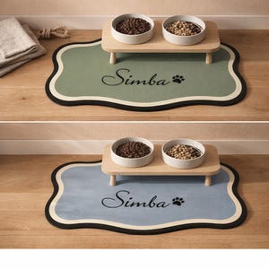 May include: A pet feeding station featuring two bowls on a wooden stand, placed on a green or blue mat. The mat has a black border, a white inner border, and the name "Simba" with a paw print.