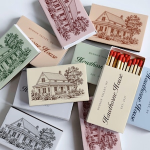 May include: A collection of rectangular matchboxes featuring illustrations of houses. Each box displays the text 'Hawthorne House', 'Hudson Valley, NY', and 'Est. 2027'. One open box reveals wooden matches with red tips. The boxes are in various pastel colors.