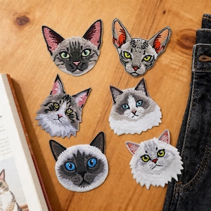 May include: A collection of embroidered cat face patches, featuring breeds like Siamese and Ragdoll. The patches display detailed stitching, showcasing different fur patterns and eye colours. Ideal for customising clothing or accessories.