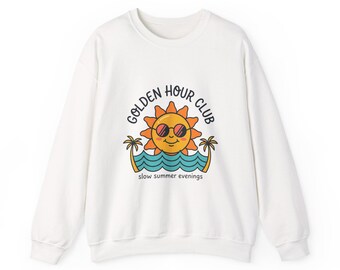 Könnte beinhalten: Weißes Sweatshirt mit einer Grafik einer lächelnden Sonne mit Sonnenbrille, dem Text "GOLDEN HOUR CLUB" und "slow summer evenings". Die Sonne befindet sich über blauen Wellen und Palmen. Ein lässiges, bequemes Oberteil.