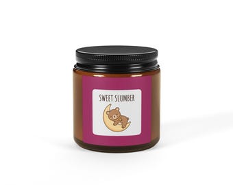 Könnte beinhalten: Eine zylindrische Kerze in einem dunkel bernsteinfarbenen Glasgefäß mit schwarzem Schraubdeckel. Das Etikett ist magentafarben mit einem weißen quadratischen Zentrum, das den Text SWEET SLUMBER und einen braunen Bären auf einem gelben Mond zeigt.