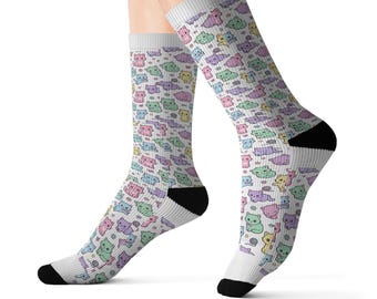 Könnte beinhalten: Ein Paar weiße Socken mit einem durchgehenden Muster aus kleinen, pastellfarbenen Cartoon-Katzen in Rosa, Grün, Blau, Lila und Gelb, akzentuiert durch winzige graue Wollknäuel und Sterne, mit einfarbig schwarzen Fersen und Zehenbereichen.