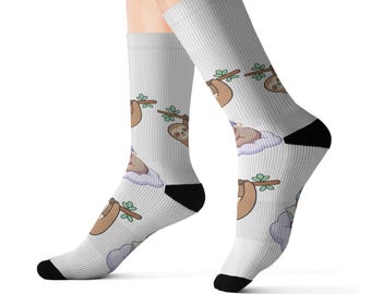 Könnte beinhalten: Ein Paar weiße Socken mit einem wiederkehrenden Muster aus braunen Faultieren, die an grünen Ästen hängen und auf hellvioletten Wolken ruhen. Die Socken haben schwarze Fersen und Zehenbereiche sowie eine durchgehend gerippte Textur.
