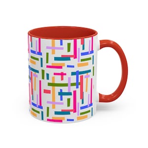 May include: White ceramic mug with a red interior and handle. The exterior features a colorful geometric pattern of rectangles in shades of pink, blue, green, orange, and purple. The mug is designed for hot beverages.