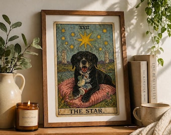 Puede incluir: Impresión artística enmarcada de una carta del tarot con un perro negro sobre un cojín rosa. La carta se titula "THE STAR" con una estrella y otros elementos celestiales. La impresión está en un marco de madera, con una vela, libros y una taza.