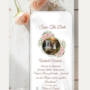 May include: A digital Save the Date card featuring a central circular photo of a proposal, framed by pink flowers and green leaves. The text reads Save The Date, Verliebt, Verlobt, Olivia & Samuel, 12.Juni.2026 München, and a German message.