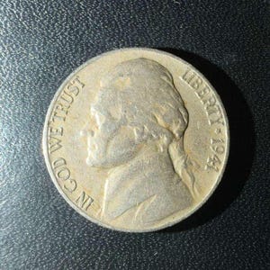 Puede incluir: Una moneda plateada con el perfil de un hombre, la inscripción "LIBERTY" y el año "1944". La moneda también presenta la inscripción "IN GOD WE TRUST".