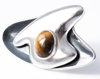 May include: A silver ring featuring a brown tiger's eye stone set within an abstract, contemporary design.