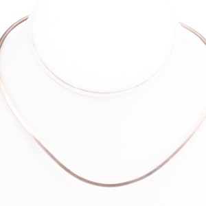 May include: A silver necklace with a simple, curved design. The necklace is made of a thin, smooth metal and has a delicate, minimalist look.