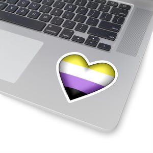 以下が含まれることがあります： ノンバイナリープライドフラッグの色をしたハート型のステッカー。フラッグは黄色、白、紫、黒です。