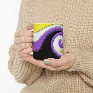Puede incluir: Una taza de cerámica blanca con un diseño abstracto colorido. El diseño presenta un remolino de amarillo, blanco, morado y negro.