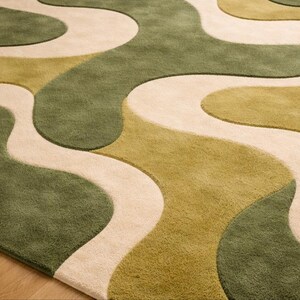 May include: A close-up of a rug with a flowing, abstract design. The rug features a pattern of interconnected, organic shapes in shades of green and beige. The rug's texture appears soft and plush, suitable for home decor.