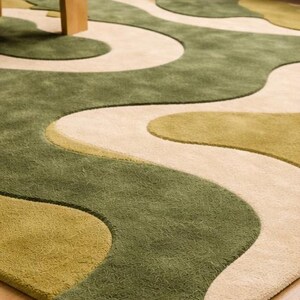 May include: A green, beige, and olive-colored area rug with a flowing, abstract design. The rug features a soft, textured surface and a modern aesthetic, suitable for living rooms or bedrooms.