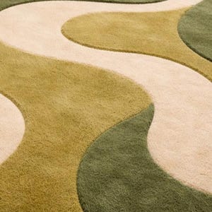 May include: Close-up of a rug with a wavy pattern in shades of green and beige. The rug has a soft, textured surface, with the design resembling flowing organic shapes. The color palette is neutral and earthy.