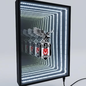 May include: Black framed infinity mirror with a team logo featuring a black eagle, a shield, and the text "BJK 1903". The mirror has white LED lights creating a tunnel effect. A black power cord is attached.