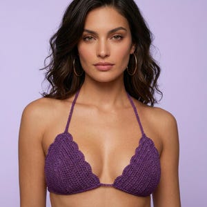 May include: A purple crochet bikini top featuring a triangular silhouette with scalloped edges along the neckline. The garment is constructed with a textured knit pattern and includes thin halter-style straps that tie behind the neck.