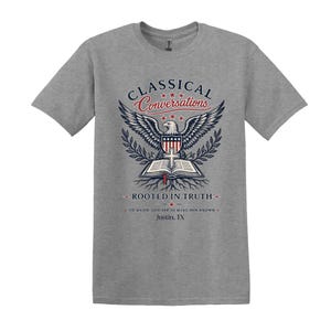May include: A heather gray short-sleeve t-shirt featuring a graphic of an eagle with wings spread above an open book and a cross. The text reads CLASSICAL CONVERSATIONS, ROOTED IN TRUTH, TO KNOW GOD AND TO MAKE HIM KNOWN, and Justin, TX.