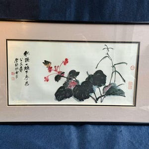 Puede incluir: Pintura de acuarela enmarcada con un arreglo floral con una mariposa. La obra de arte incluye hojas negras, flores rojas y tallos. La pintura está en un marco negro con un passe-partout rosa claro e incluye caligrafía asiática.
