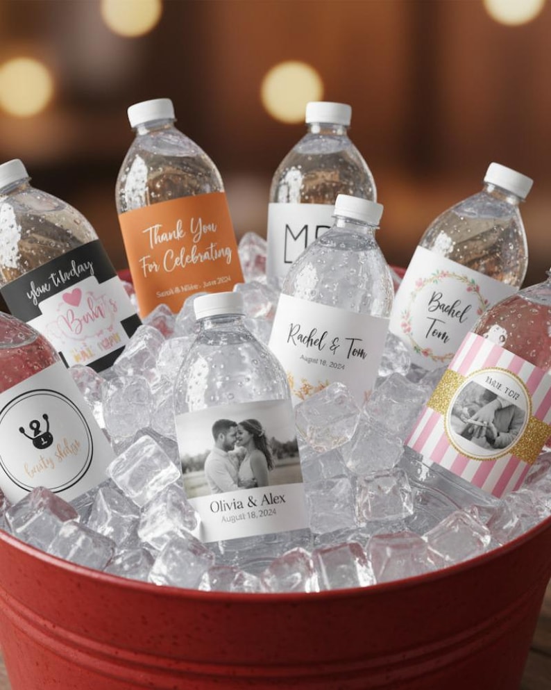 May include: Clear plastic water bottles with custom labels featuring various designs, including names, dates, and photographs, nestled in a red bucket filled with ice cubes. The labels display text such as Thank You For Celebrating, Rachel & Tom, and Olivia & Alex.