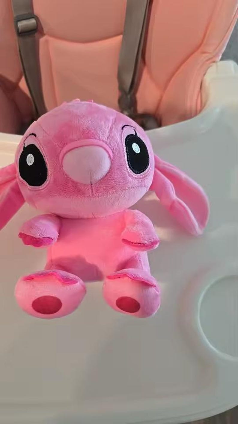 Puede incluir: Un peluche rosa de un personaje con grandes ojos negros, orejas largas y una nariz peque&ntilde;a. El juguete tiene una textura suave y difusa y est&aacute; sobre una superficie blanca. Los pies y las manos del juguete tienen acentos rosas m&aacute;s oscuros.