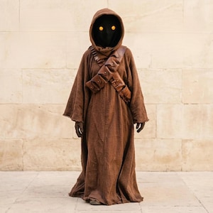 May include: A brown hooded robe costume with a black face covering and glowing yellow eyes. The costume features a brown leather bandolier across the chest and brown gloves. The costume is inspired by a science fiction film character.