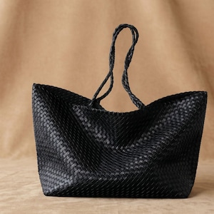 May include: A black tote bag featuring an intricate woven pattern across the entire exterior surface. The bag includes two long, slender braided handles attached to the top edge, providing a consistent texture throughout the design.