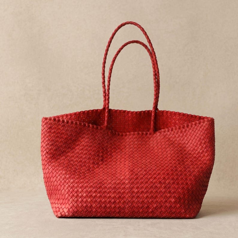 May include: A vibrant red tote bag featuring a detailed woven texture throughout the entire body. The bag includes two matching braided handles attached to the top edge, providing a consistent look with the main woven structure of the bag.