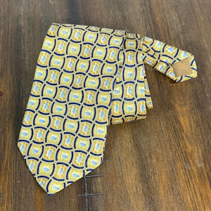 May include: A yellow tie with a repeating pattern of blue and gold shapes. The tie is made of a smooth fabric and is laying on a wooden surface. The tie is knotted and ready to wear.