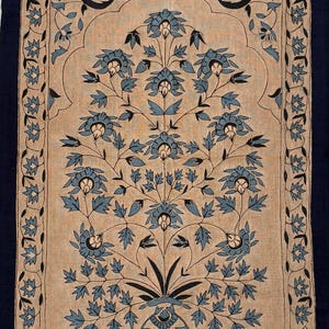 Könnte beinhalten: Ein rechteckiger textiler Wandbehang mit beigem Hintergrund und einem zentralen blauen Blumenmotiv in einer Vase. Das Design umfasst symmetrische Zweige, Blätter und Blüten, eingerahmt von einem dunkelblauen Rand mit Blattmuster.