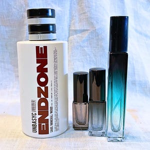 May include: A large white cylindrical bottle labeled ENDZONE SAGE/MINERAL/WOOD 3.4oz 100ml with a black and white striped cap, alongside two small square glass spray bottles with black caps and one tall rectangular teal gradient glass bottle.