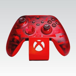 May include: Red Xbox controller and stand. The controller has a transparent red finish with dark red accents. The stand features the Xbox logo. The controller is designed for gaming.