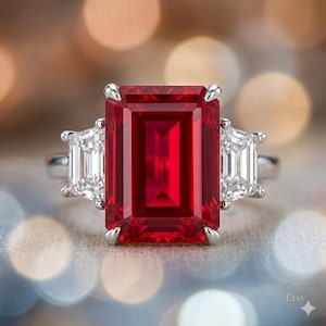 Può includere: Un anello d'argento con una grande gemma rettangolare rosso intenso affiancata da due gemme chiare rettangolari più piccole. Il design dell'anello è elegante e classico, con un focus sul colore vibrante della pietra centrale.