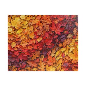 May include: A rectangular jigsaw puzzle featuring a dense, high-angle photographic print of fallen autumn leaves. The composition displays a vibrant gradient of colors, transitioning from bright yellow and gold to deep orange, red, and dark maroon.