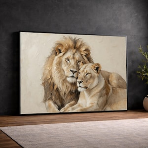 Pode incluir: Uma peça de arte de parede retangular com uma pintura a óleo texturizada de um leão com uma juba cheia descansando ao lado de uma leoa. A obra é feita em tons de creme, bege e marrom dourado, dentro de uma moldura preta fina.