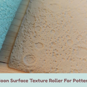 Puede incluir: Un rodillo de textura cilíndrico de color azul claro para cerámica con un patrón de superficie lunar en relieve con cráteres y protuberancias, junto a una losa de arcilla beige que muestra la textura lunar impresa.