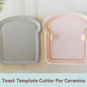 May include: Two bread-shaped template cutters for ceramics, one in solid gray and one in light pink with a white outer frame. Each cutter features a flat, smooth surface with a raised border in the shape of a slice of toast. The text Toast Template Cutter For Ceramics is printed below the items.