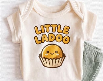 May include: A cream-colored ribbed baby bodysuit featuring the text "LITTLE LADOO" in bold yellow letters above a graphic of a smiling yellow round sweet in a brown paper liner, paired with sage green ribbed pants.