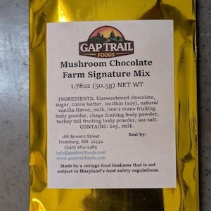 Könnte beinhalten: Eine goldene Folienverpackung von Gap Trail Foods Mushroom Chocolate Farm Signature Mix. Das Etikett enthält den Produktnamen, das Nettogewicht von 50,5 g und eine Zutatenliste. Die Verpackung enthält auch die Adresse und die Website des Unternehmens.