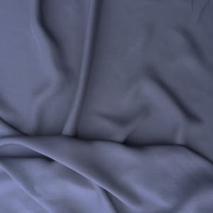 May include: A close-up shot of a draped fabric in a muted blue-purple hue. The material has soft folds and subtle shadows, creating a sense of depth and texture. The fabric appears smooth and flowing, suggesting a lightweight material.